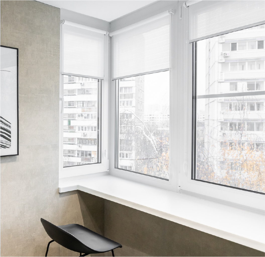 Рулонная штора INTEGRA SLIM (белая) на створке окна лоджии. Общий вид: пластиковые рамы, ткань создает мягкое рассеивание света.